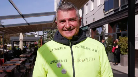 Guy Delauney/BBC A man in a yellow top with the legend Students Win written in Serbian