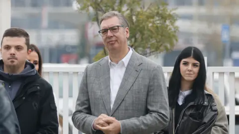 EPA Aleksandar Vucic in a grey suit and white shirts waits in a  polling station queue