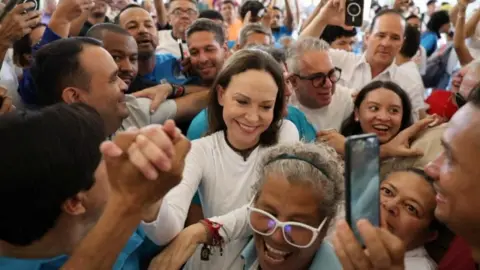 Reuters A woman in white with long brown hair is surrounded by smiling, enthusiastic people, one of whom is clasping her hand