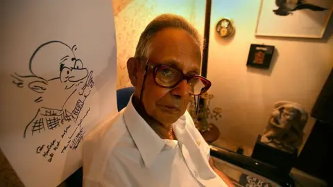 India Today Group via Getty Images RK Laxman, Cartoonist with a sketch of his most famous character 'Common Man' at his Residence in Mumbai, Maharashtra, India 