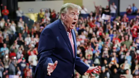Reuters US President Donald Trump at a rally in support of Republican US Senate reelection candidate Roger Marshall in Kansas on 19 October. He wears a blue suit, white shirt and red and white patterned tie