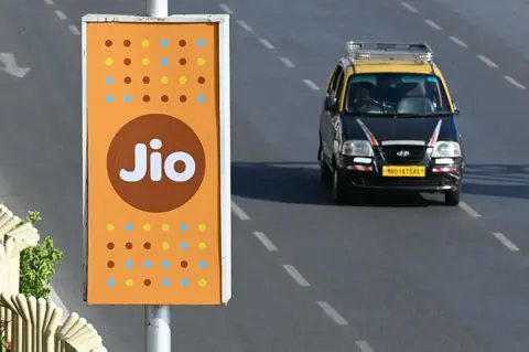 AFP via Getty Images A black and yellow Mumbai taxi rides past a Jio advertisement in Mumbai. 