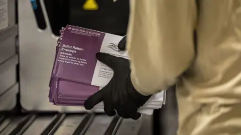 Getty Images An election worker wearing gloves holding a batch of postal ballots in envelopes