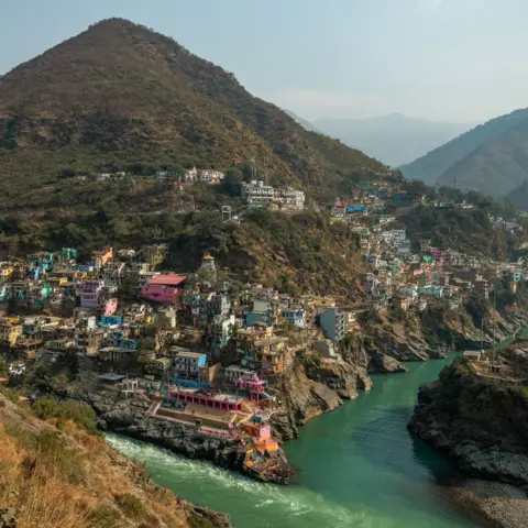 Bloomberg The turquoise waters of two rivers meet at Devprayag in the Indian Himalayan state of Uttarakhand, with colourful buildings clustered on steep rocky hillsides above the confluence. Surrounded by rugged mountains, the rivers wind through a narrow valley lined with temples, homes and roads carved into the slopes.