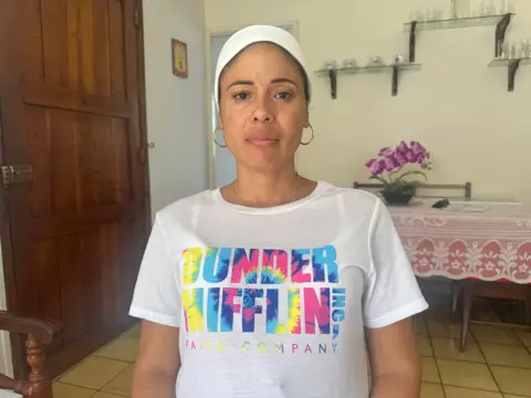 Heydi Sanchez looks at the camera while standing in her kitchen, wearing a brightly coloured t-shirt