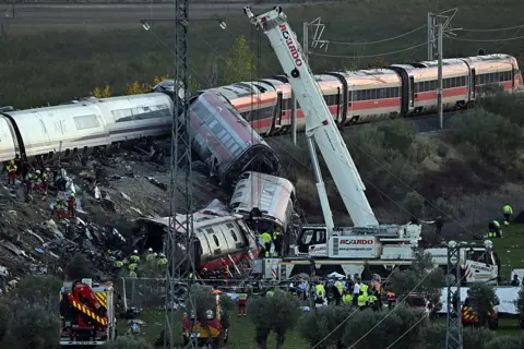 AFP via Getty Images A crane at the site of the train crash near Urda on 28 October. A number of one train's carriages have fallen down a ledge, while other carriages remain on the railway line.