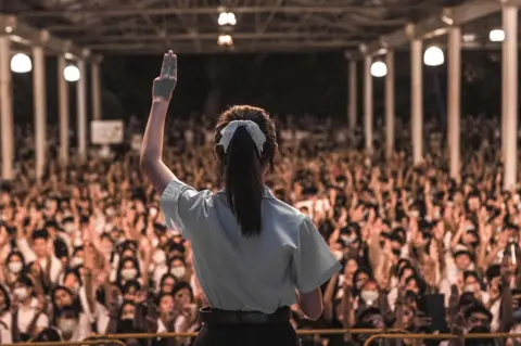 Goodmondayshoot Supitcha Melinn Chailom doing the three-finger salute in August 2020 in front of a crowd of protesters
