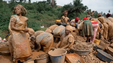 AFP via Getty Images A group of women covered in mud next to buckets of stones and dirt