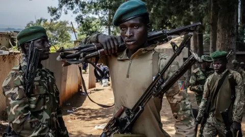 Getty A man wearing combat uniform carries AK 47 guns on his shoulder supported his right hand with another gun hanging across his chest flanked by 3 other solders in the background