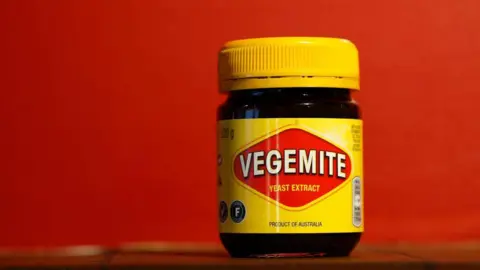 Getty Images A yellow jar of Vegemite on a shelf, with a red background