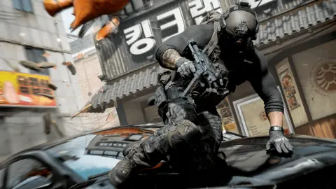 Activision A still from Call of Duty Modern Warfare 4 showing a soldier leaping over a car on a South Korean street. He wears a helmet and protective gear and is armed with a large gun. 