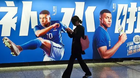 CFOTO/Future Publishing via Getty Images Pedestrians pass by an electrolyte drink advertisement for French football player Kylian Mbappé in the subway in Shanghai, China on June 30, 2026