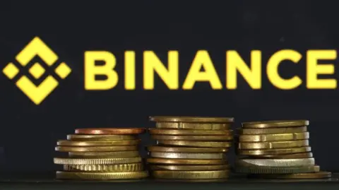 Getty Images In this photo illustration, the Binance logo is displayed on a screen behind a stack of gold coins.
