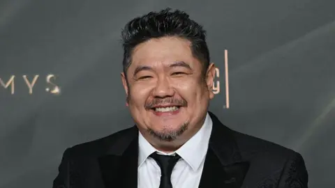 AFP via Getty Images A man in a dark suit with a close-cropped goatee smiles at a premiere