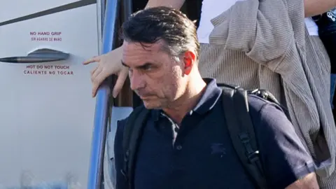 Getty Images Bolsonaro in a dark shirt carrying a backpack as he leaves a plane