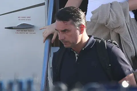 Getty Images Bolsonaro in a dark shirt carrying a backpack as he leaves a plane