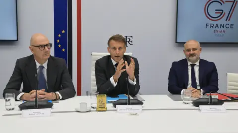 Reuters French President Emmanuel Macron (C) speaks next to France's Economy, Finance and Industry Minister Roland Lescure and Secretary-General of the Office of the President of the French Republic Pierre-Andre Imbert following a video conference with G7 leaders