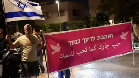 AFP via Getty Images People demonstrate holding a banner that says "Love your neighbour" in Arabic and Hebrew