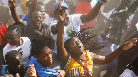 Reuters A group of young people at a rally. The main focus is a woman with a yellow Chicago Bulls basketball vest. She has her eyes closed, her arms outstretched and her hair is waving behind her while she jumps up and down