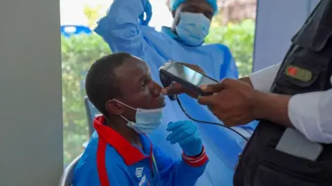 EPA/Shutterstock A man getting checked by a health professional who holds an implement up to him
