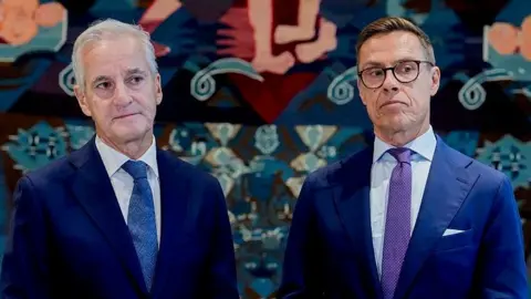 AFP via Getty Images Norway's Prime Minister Jonas Gahr Støre (L) and Finnish President Alexander Stubb wearing navy suits. Støre has a white shirt and blue tie, while Stubb has a white shirt, purple tie and black-rimmed glasses. 