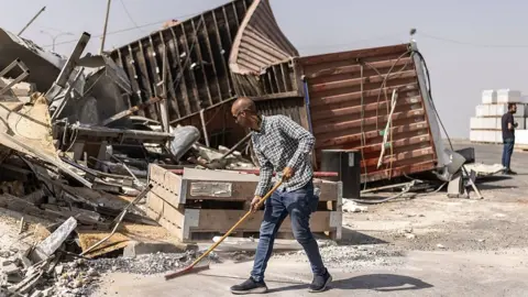 AFP via Getty Images Man sweeps up debris. 