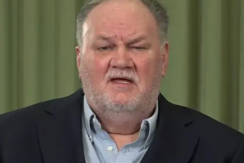 ITV / Shutterstock Close-up of Thomas Markle Sr wearing a dark blazer and light blue shirt, against a green curtain backdrop