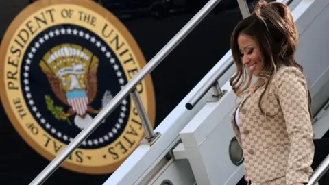 Reuters Minaj, smiling in her gold suit, walks down the steps of Air Force one, with the plane's livery clear in the background. 