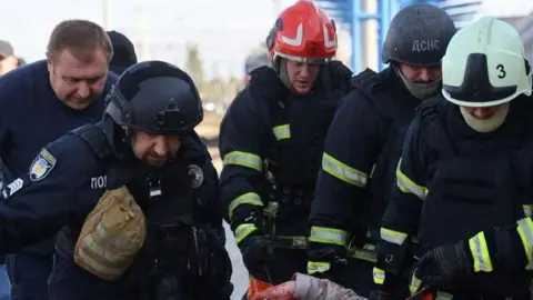 State Emergency Service Of Ukraine A group of men carry an injured person, who is out of shot, from a railway station after a strike in Dnipro.