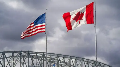 Getty Images The US and Canada flags flutter next to the Blue Water Bridge border crossing in Point Edward, Ontario, on 24 October 2025. 